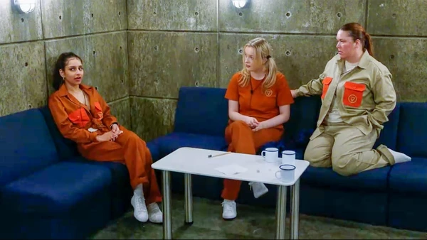 Participants in prison - style outfits interact in a room in "Rise and Fall".