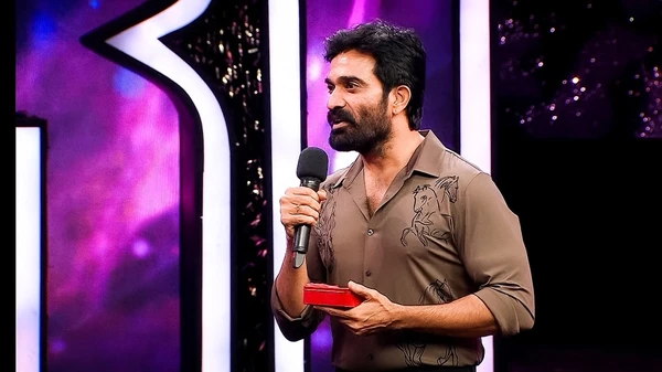The host of "Bigg Boss Telugu" holds a microphone and a box during the show.