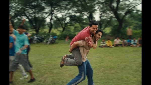 One man carries another on his back while playing on a field in Homebound.
